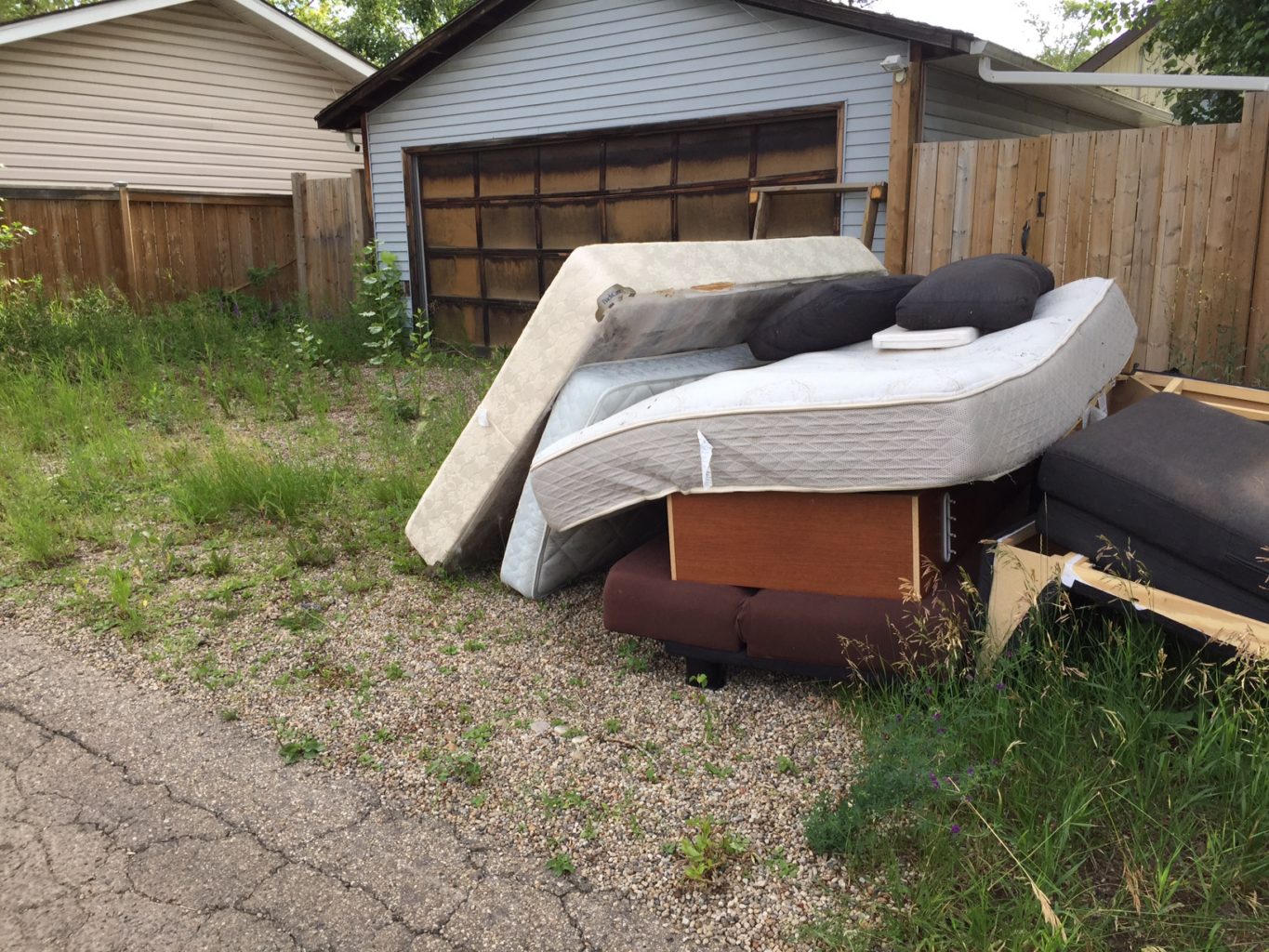 Household junk of some mattresses and a couch, behind a garage.