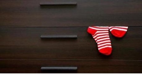 Striped red socks hang out of a brown wooden dresser.